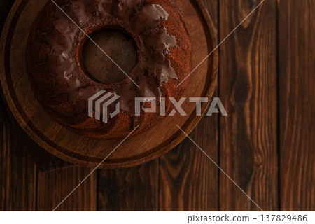 Chocolate cake with chocolate icing on dark wooden table. Low key. Top view Chocolate cake with chocolate icing on dark wooden table. Low key. Top view 137829486