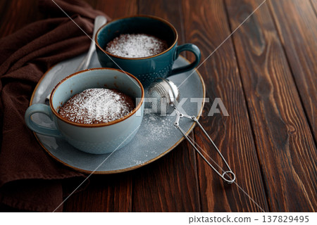 Two chocolate mug cake under sugar icing on dark wooden table. Easy homemade dessert. Mugcake from microwave Two chocolate mug cake under sugar icing on dark wooden table. Easy homemade dessert. Mugcake from microwave 137829495