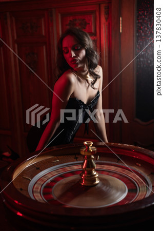A beautiful brunette in a black dress at the casino roulette wheel.  137830408