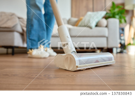 Closeup of cordless vacuum cleaner head on floor with woman in background Closeup of cordless vacuum cleaner head on floor with woman in background 137830843