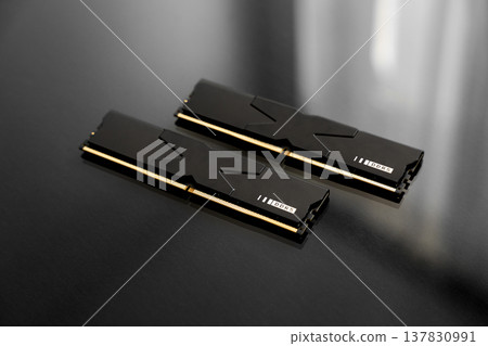 Black DDR5 RAM memory modules placed on a dark, glossy surface. RAM shortages on the market, rising prices, and increased demand driven by the growing need for AI training. Black DDR5 RAM memory modules placed on a dark, glossy surface. RAM shortages on the market, rising prices, and increased demand driven by the growing need for AI training. 137830991