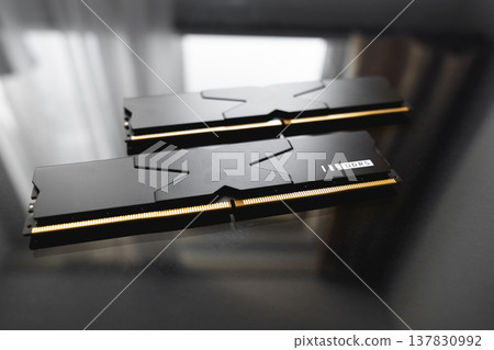 Black DDR5 RAM memory modules placed on a dark, glossy surface. RAM shortages on the market, rising prices, and increased demand driven by the growing need for AI training. Black DDR5 RAM memory modules placed on a dark, glossy surface. RAM shortages on the market, rising prices, and increased demand driven by the growing need for AI training. 137830992