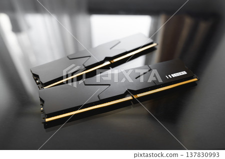 Black DDR5 RAM memory modules placed on a dark, glossy surface. RAM shortages on the market, rising prices, and increased demand driven by the growing need for AI training. Black DDR5 RAM memory modules placed on a dark, glossy surface. RAM shortages on the market, rising prices, and increased demand driven by the growing need for AI training. 137830993
