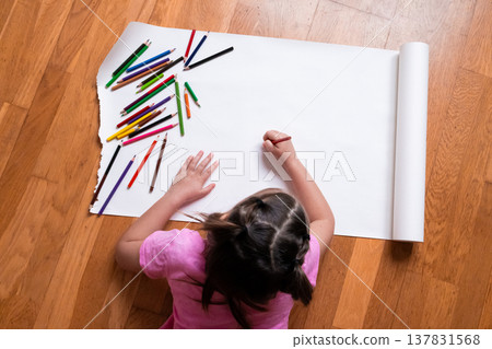 Young female child drawing with pencils on large white paper on wooden floor Young female child drawing with pencils on large white paper on wooden floor 137831568