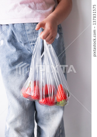 Child holding bag of fresh strawberries in clear plastic bag Child holding bag of fresh strawberries in clear plastic bag 137831575