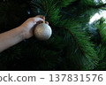 Child hand placing silver ornament on Christmas tree branch 137831576