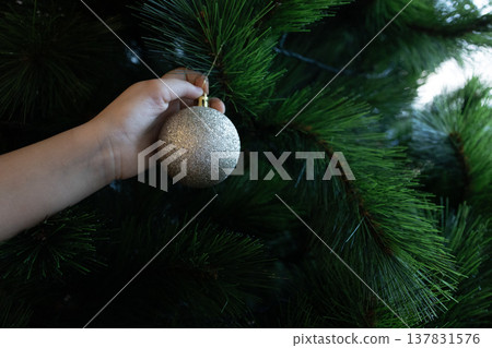 Child hand placing silver ornament on Christmas tree branch 137831576