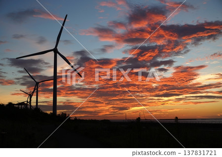 A vibrant sunset sky and the silhouette of wind turbines. A vibrant sunset sky and the silhouette of wind turbines. 137831721