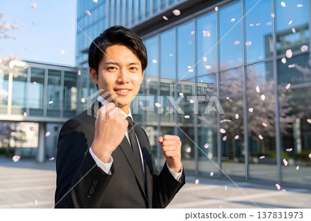 一位穿著西裝的日本男子站在公司大樓前，櫻花飄落，他正在為自己打氣。圖片為新進員工形象（AI生成）。 137831973