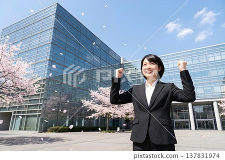 一位身著職業套裝的日本女性站在公司大樓前,周圍櫻花飄落,她正為即將到來的場合做準備。圖片為新進員工形象(人工智慧生成)。 一位身著職業套裝的日本女性站在公司大樓前,周圍櫻花飄落,她正為即將到來的場合做準備。圖片為新進員工形象(人工智慧生成)。 137831974