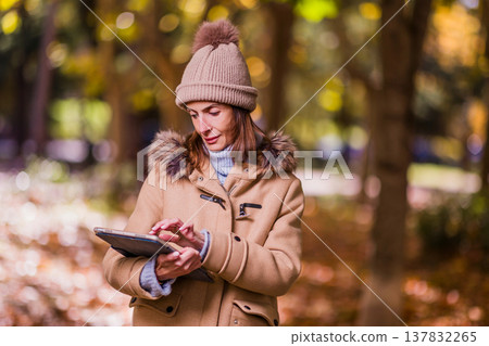Woman with anorexia using touch screen tablet in autumn park Woman with anorexia using touch screen tablet in autumn park 137832265
