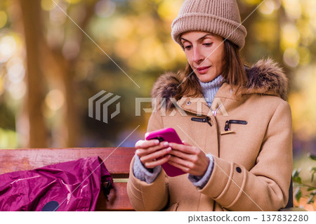 Woman with anorexia using smartphone outdoors on park bench Woman with anorexia using smartphone outdoors on park bench 137832280