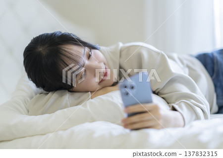 A young woman lying down and staring at her smartphone screen 137832315