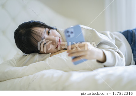 A young woman lying down and staring at her smartphone screen 137832316