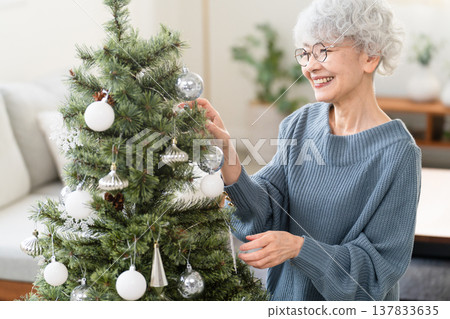 Senior woman decorating Christmas tree with ornaments Senior woman decorating Christmas tree with ornaments 137833635