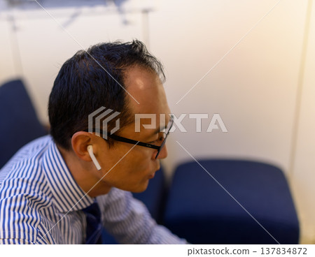 一位戴著眼鏡、戴著耳機的中年商務人士的側臉。 137834872