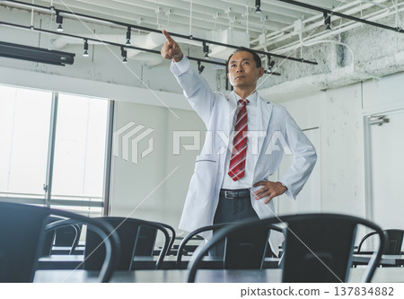 A male doctor in a white coat points in the room. A male doctor in a white coat points in the room. 137834882