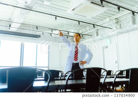 A male doctor in a white coat points in the room. 137834900