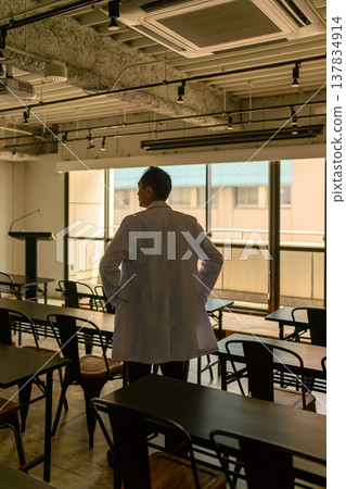 A male doctor in a white coat is seen with his back to the window. 137834914