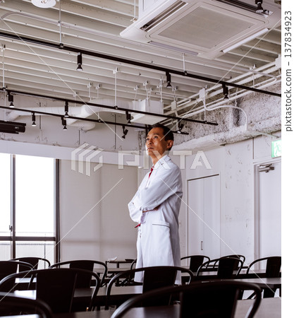 A specialist in a white coat stands in a brightly lit room. 137834923