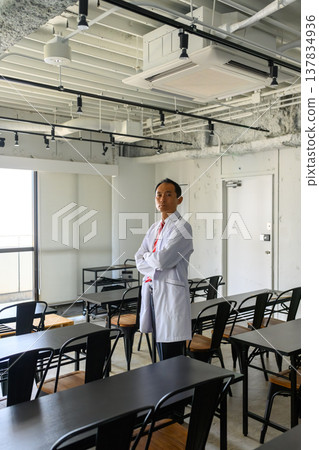 A male doctor in a white coat crosses his arms in the classroom. A male doctor in a white coat crosses his arms in the classroom. 137834936
