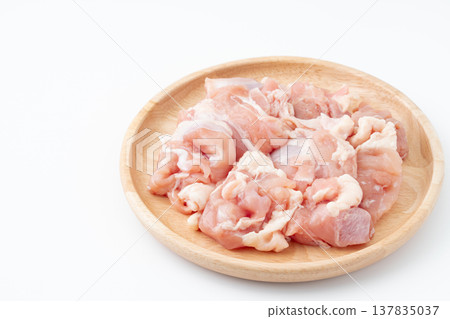 Raw chicken thigh pieces on a wooden plate against a white background. 137835037