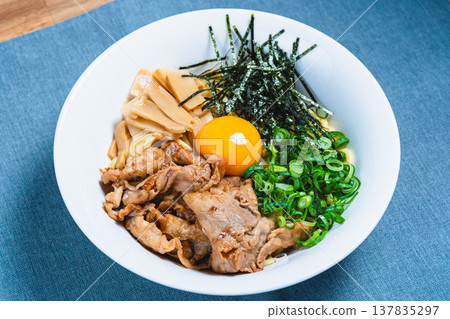 Oil noodles topped with pork and a raw egg; homemade mixed noodles on the table. Oil noodles topped with pork and a raw egg; homemade mixed noodles on the table. 137835297