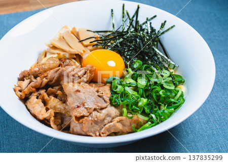 Oil noodles topped with pork and a raw egg; homemade mixed noodles on the table. 137835299