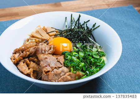 Oil noodles topped with pork and a raw egg; homemade mixed noodles on the table. 137835483