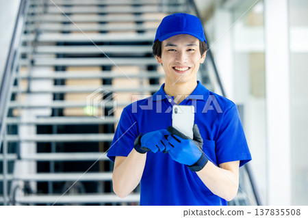 倉庫裡的一名男性工人手持智慧型手機。 倉庫裡的一名男性工人手持智慧型手機。 137835508