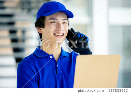 A male worker in a warehouse holding a smartphone. A male worker in a warehouse holding a smartphone. 137835512