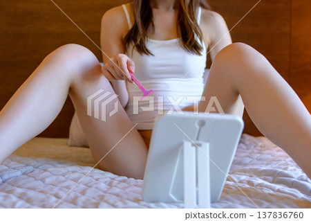 一位年輕女子正在對著鏡子用剃刀刮陰毛,修剪腹股溝(比基尼區域)的毛髮,進行自我照顧。 一位年輕女子正在對著鏡子用剃刀刮陰毛,修剪腹股溝(比基尼區域)的毛髮,進行自我照顧。 137836760