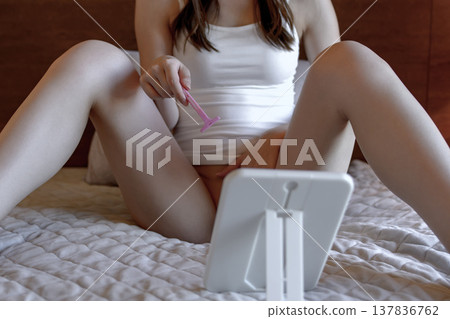 一位年輕女子正在為自己的陰道、大腿內側和肛門區域進行自我護理,對著鏡子剃毛、加深毛髮顏色並修剪毛髮。 一位年輕女子正在為自己的陰道、大腿內側和肛門區域進行自我護理,對著鏡子剃毛、加深毛髮顏色並修剪毛髮。 137836762