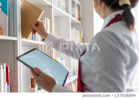 一位女士拿出一本書，在平板電腦上查看。 137836804
