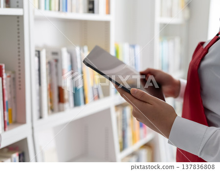 A store clerk checking a tablet device in a bookstore. 137836808