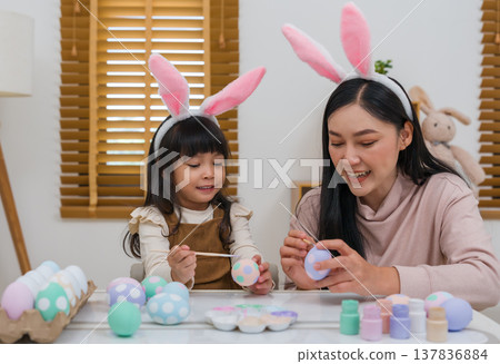 mother and preschool child girl wearing bunny ears painting and decorating egg together at home on easter day. happy family holiday activity concept mother and preschool child girl wearing bunny ears painting and decorating egg together at home on easter day. happy family holiday activity concept 137836884