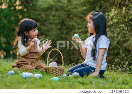 two child girl playing together and hunting for Easter eggs into basket on green grass in garden two child girl playing together and hunting for Easter eggs into basket on green grass in garden 137836913