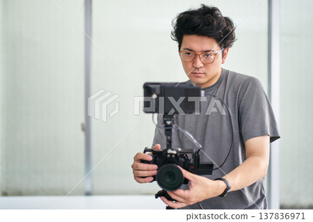 A man wearing glasses and a T-shirt is filming a video indoors. 137836971