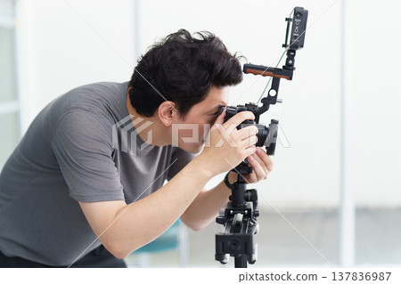 片場一名男子手持無反光鏡相機,透過觀景窗檢查對焦情況,然後開始拍攝影片。 片場一名男子手持無反光鏡相機,透過觀景窗檢查對焦情況,然後開始拍攝影片。 137836987