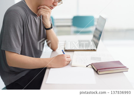 一名男子正在參加認證課程，用電腦和筆做筆記。 137836993