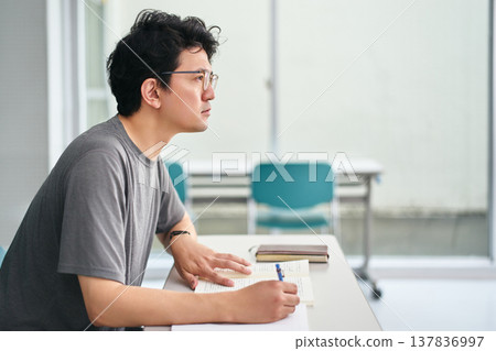 一名男學生正在教室裡認真聽講,手裡拿著課本,一邊聽一邊做筆記。 一名男學生正在教室裡認真聽講,手裡拿著課本,一邊聽一邊做筆記。 137836997