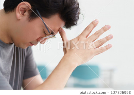 一位三十多歲的日本男子側臉，戴著眼鏡，手扶額頭，陷入沉思。 137836998