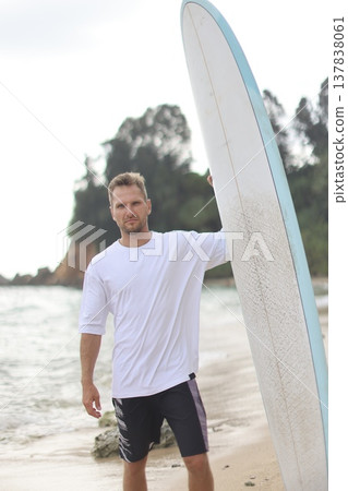 Casual Model Posed Beside Surfboard By Ocean. Photograph Of Woman In T Shirt With Surfboard At Beach Casual Model Posed Beside Surfboard By Ocean. Photograph Of Woman In T Shirt With Surfboard At Beach 137838061
