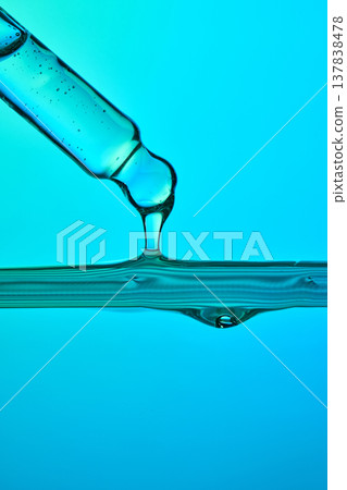 Dropper dispensing liquid serum onto a clear blue surface Dropper dispensing liquid serum onto a clear blue surface 137838478