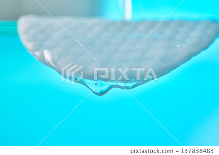 Cotton pad soaking, dripping gel on blue background Cotton pad soaking, dripping gel on blue background 137838483