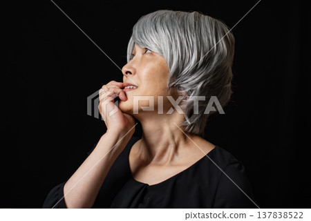 An elderly woman, with her hand to her mouth, lost in thought. An elderly woman, with her hand to her mouth, lost in thought. 137838522