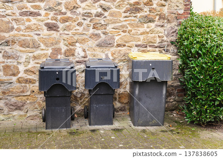 Household garbage and recycling bins near stone wall in typical German residential neighborhood 137838605