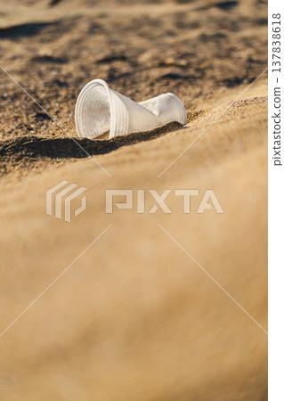 Plastic disposable cup discarded on sandy beach representing pollution and human impact on nature 137838618