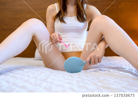 一位年輕女子在臥室裡對著手鏡,用 T 型剃刀刮比基尼部位的毛髮,進行自我照顧。 一位年輕女子在臥室裡對著手鏡,用 T 型剃刀刮比基尼部位的毛髮,進行自我照顧。 137838675