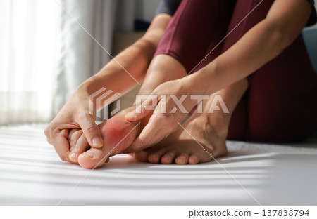 Woman massaging painful foot and toe with red highlight. Foot pain, plantar fasciitis, gout, arthritis and peripheral neuropathy concept for health care, physical therapy and medical treatment. 137838794